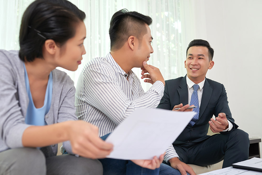 Smiling Vietnamese real estate broker consulting young couple at meeting